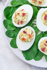 Deviled eggs stuffed with avocado, egg yolk and mayonnaise filling, garnished with bacon, on spinach leaves, vertical, top view closeup