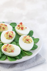 Fototapeta na wymiar Deviled eggs stuffed with avocado, egg yolk and mayonnaise filling, garnished with bacon, on spinach leaves, vertical copy space