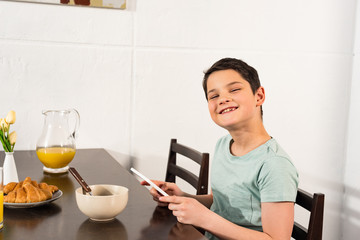 smiling boy using digital tablet during breakfast in kitchen
