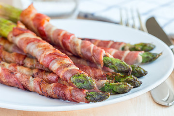 Green asparagus wrapped with bacon on  white plate, horizontal