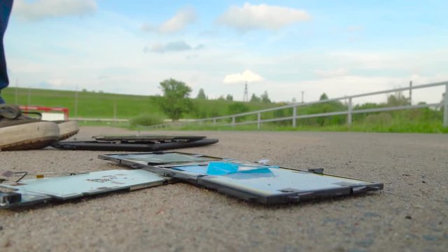 A man walks along the road and injures the tablet, the phone falls to the surface of the road and breaks into smithereens. Slow motion. The guy is upset.