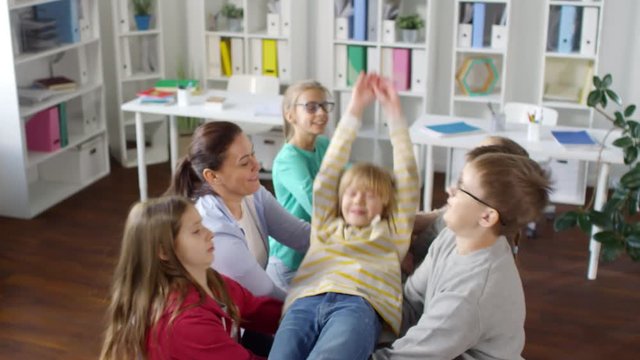 High-angle shot of smiling blond teenage boy slowly falling backwards and other kids with female teacher catching him, while standing in pairs and gripping each other&rsquo;s hands