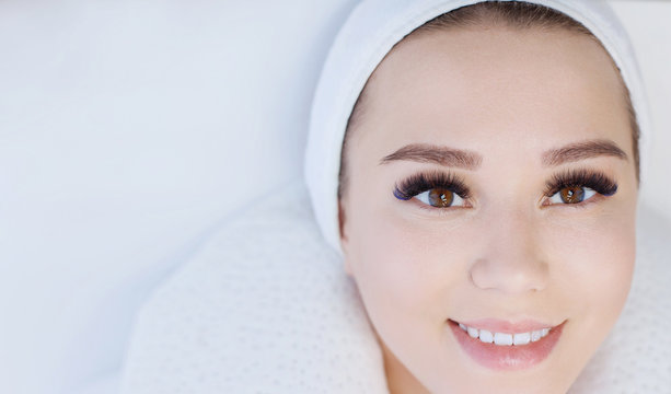 Eyelash extension procedure. Beautiful woman with long eyelashes and perfect glow clean skin. Girl in beauty salon getting facial treatment. Perfect trendy eyebrows.