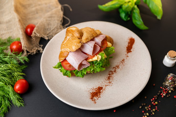 Breakfast croissant sandwich with ham and cheese. Top view. black background with vegetables. Slow-mo.