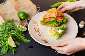 Breakfast Croissants with soft cheese, salted salmon and green salad. Love. Top view. black background with vegetables. Slow-mo.