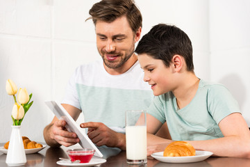 smiling father and son using digital tablet during breakfast