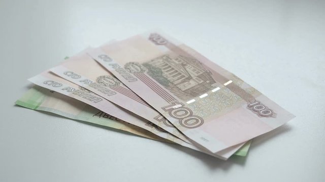To count money. Money falls on a white table. People hand throws russian rubles banknotes nominals 200 and 100 and coins nominal 10 on a white background