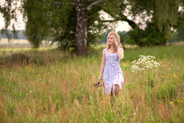 Rural, rural life. Walking through the meadow blonde young woman in a hat. Summertime.