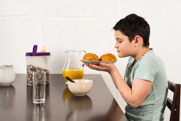 boy sniffing croissants with closed eyes during breakfast in kitchen