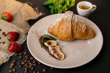 Tasty breakfast. Croissant with banana, peanut butter and chocolate. Black background. Slow-mo.