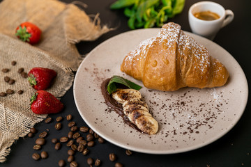 Tasty breakfast. Croissant with banana, peanut butter and chocolate. Black background. Slow-mo.