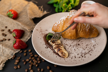 Tasty breakfast. Croissant with banana, peanut butter and chocolate. Black background. Slow-mo.