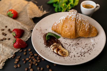 Tasty breakfast. Croissant with banana, peanut butter and chocolate. Black background. Slow-mo.