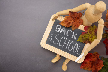 wood mannequin holding chalkboard  with words back to school and piece of chalk sitting on a...