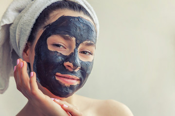 Beauty portrait of woman in towel on head applying black nourishing mask on face, white background isolated. Skincare cleansing eco organic cosmetic spa relax concept
