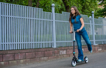 Outdoor portrait of young teenager brunette girl with long hair driving scooter on city street