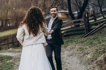 stylish, attractive bearded bridegroom gives a hand to the bride inviting her to go along with him in the mountain road