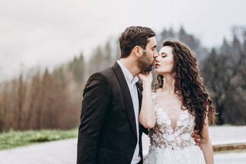 Slender graceful bride in a wedding dress kisses her stylish bride touching her face to face. Perfect wedding couple