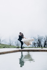 Obraz premium a stylish wedding couple photo, a man spins his bride by holding his hands near the pool in the mountains, a pair of reflections visible in the water