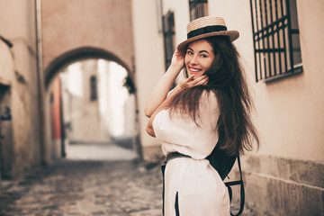 Fototapeta premium Young stylish woman walking on the old town street, travel with backpack, straw hat, wearing trendy outfit.