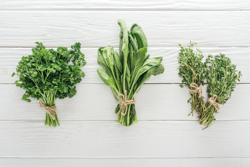 top view of green parsley, basil and thyme on white wooden table