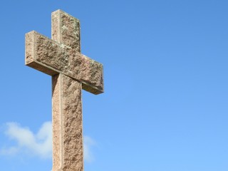 Scene in a graveyard: close-up of a religious stone cross illuminated by the sun. Blue sky on a sunny day. Faith and religiosity.