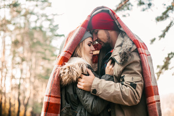 Couple huggings travelers covered with plaid in the forest. Concept of trekking, adventure and seasonal vacation.