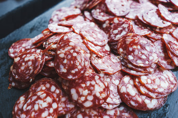 Thinly sliced sausage slices on a black stone board. 