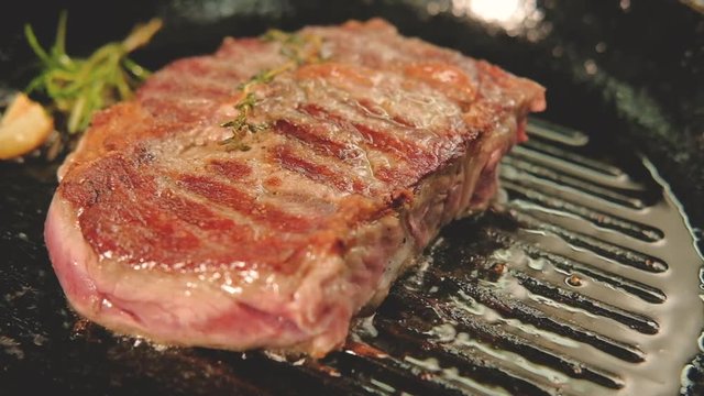 Grilled meat recipe. Steak portion cooking on frying pan with rosemary and garlic