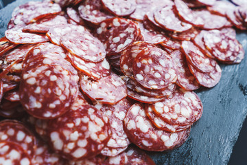 Thinly sliced sausage slices on a black stone board. 