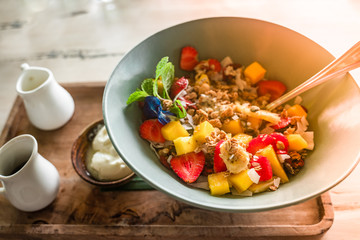 Healthy breakfast porridge concept: oatmeal with coconut flakes, strawberry, banana and mango pieces served with Greek yogurt and natural honey decorated with mint and flowers.