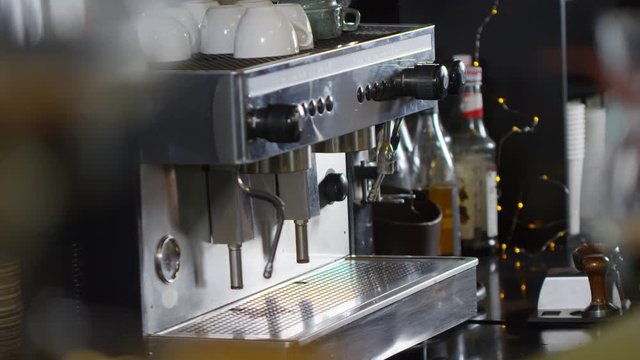 Close-up shot of coffee machine and tattooed barista pouring ground coffee from doser into portafilter, tamping it, inserting portafilter into group, placing cup underneath and start brewing espresso