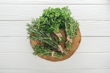 top view of green parsley, rosemary and thyme on brown stump on white wooden table