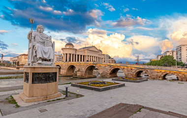 SKOPJE, NORTH MACEDONIA - 25.04.2019: Byzantine Emperor Justinian Statue and Stone Bridge, behind the Archeology Museum at sunset in Skopje - obrazy, fototapety, plakaty