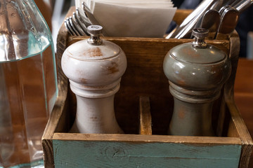 Stylish wooden salt and pepper mills in a wooden crate on a restaurant table