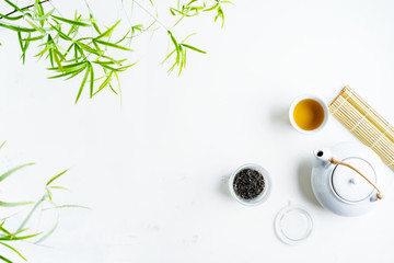 Fototapeta premium Asian tea concept, two white cups of tea and teapot surrounded with green tea dry leaves view from above, space for a text on white background.