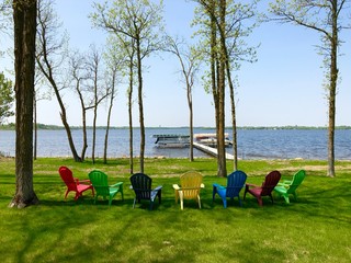 Colorful lawn chairs on green grass near lake shore with boat and pontoons on lifts at dock on a...