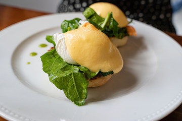 Egg Benedict with salmon and fresh spinach served under hollandaise sauce on a white plate