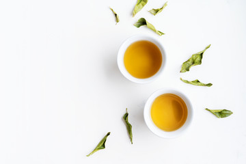 Obraz na płótnie Canvas Asian tea concept, two white cups of tea and teapot surrounded with green tea dry leaves view from above, space for a text on white background.