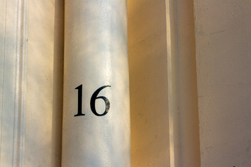 House number 16 with the sixteen in black on a cream colored pillar or column