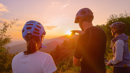 CLOSE UP: Unrecognizable mountain biker pointing at the beautiful golden sunset.