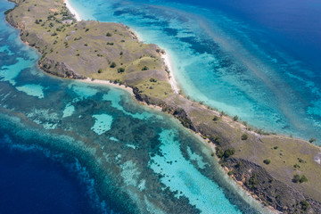 Obraz na płótnie Canvas Seen from a bird's eye view, a narrow peninsula is fringed by a healthy coral reef in Komodo National Park, Indonesia. This tropical area is known for its marine biodiversity as well as its dragons.