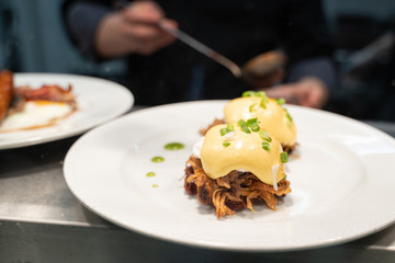 Pulled pork served on fried potato pancakes topped with poached egg and garnished with hollandaise sauce and fresh green onion aka 