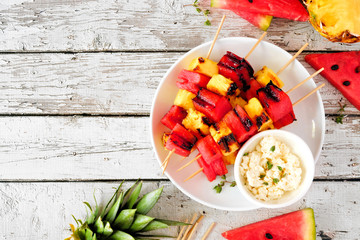 Grilled watermelon and pineapple fruit skewers with feta. Above view on a white wood table. Summer food concept.