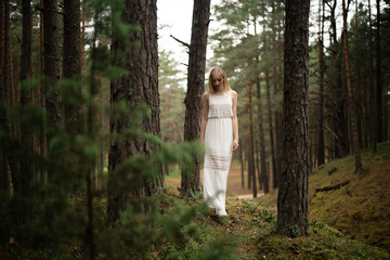 Walking Beautiful young blonde woman forest nymph in white dress in evergreen wood