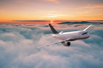 Naklejka na ściany i meble Commercial airplane jetliner flying above dramatic clouds in beautiful sunset light. Travel concept.