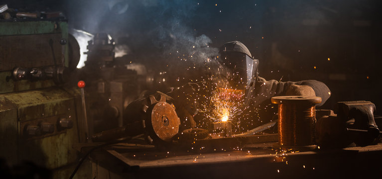 Welder is welding metal part in industrial workshop.