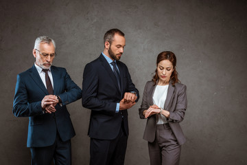 attractive businesswoman and handsome businessmen looking at watches on grey