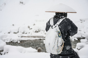 Unrecognised Japanese Ninja black dress with big hat covered by snow storm standing taking photos of snow monkeys in front of the river in the park in Japan