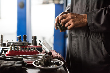 Mechanic hands holding car part next to tools